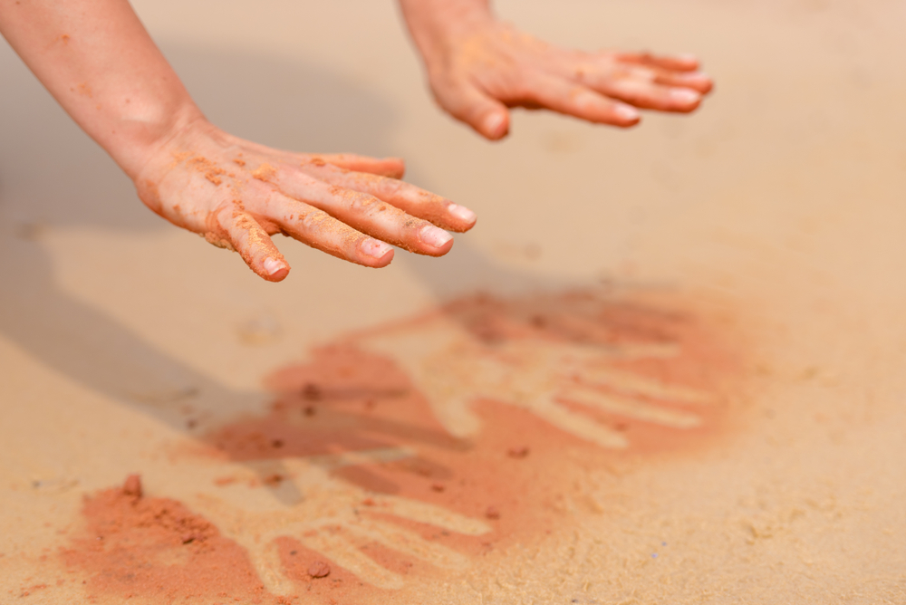 Woman,Hands,Creating,Shapes,With,Red,Sand,On,The,Beach