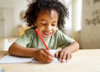 Smiling,African,American,Child,Schoolboy,Doing,Homework,While,Sitting,At