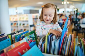 Five,Year,Old,Girl,Selecting,A,Book,In,Municipal,Library