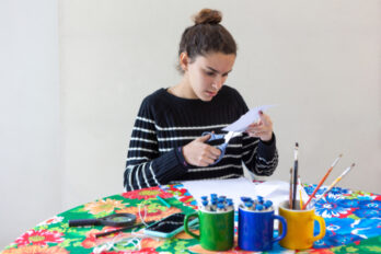 Young,Talented,Woman,Artist,Sitting,At,Flowered,Table,With,Pencils,